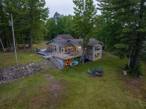 Une cabane à deux étages avec une terrasse, entourée d’arbres.