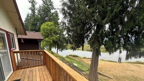 A wooden deck with a view of a lake and trees. - The Lewis River Salmon Shores - Waterfront View & Fishing,  Book It Now! (Woodland)