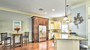 A kitchen with wooden cabinets, a stainless steel refrigerator, a marble countertop, and a hanging light fixture. - Corpus Christi Home w/ Golf Cart: Walk to Beach! (Corpus Christi)