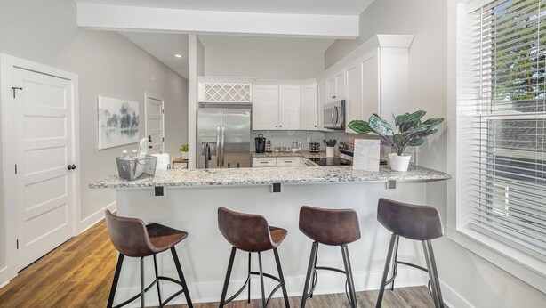 A modern kitchen with a central island, bar stools, and a large window with blinds. - Charming 1910 Luxury Condo in Downtown Fuquay - Steps to Parks & Eateries (Fuquay-Varina)