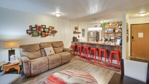A living room with a sofa, a coffee table, and a TV. There is a kitchen area with a bar and stools. - Walkable Lead Condo: 5 Mi to Terry Peak Ski Area! (Lead)