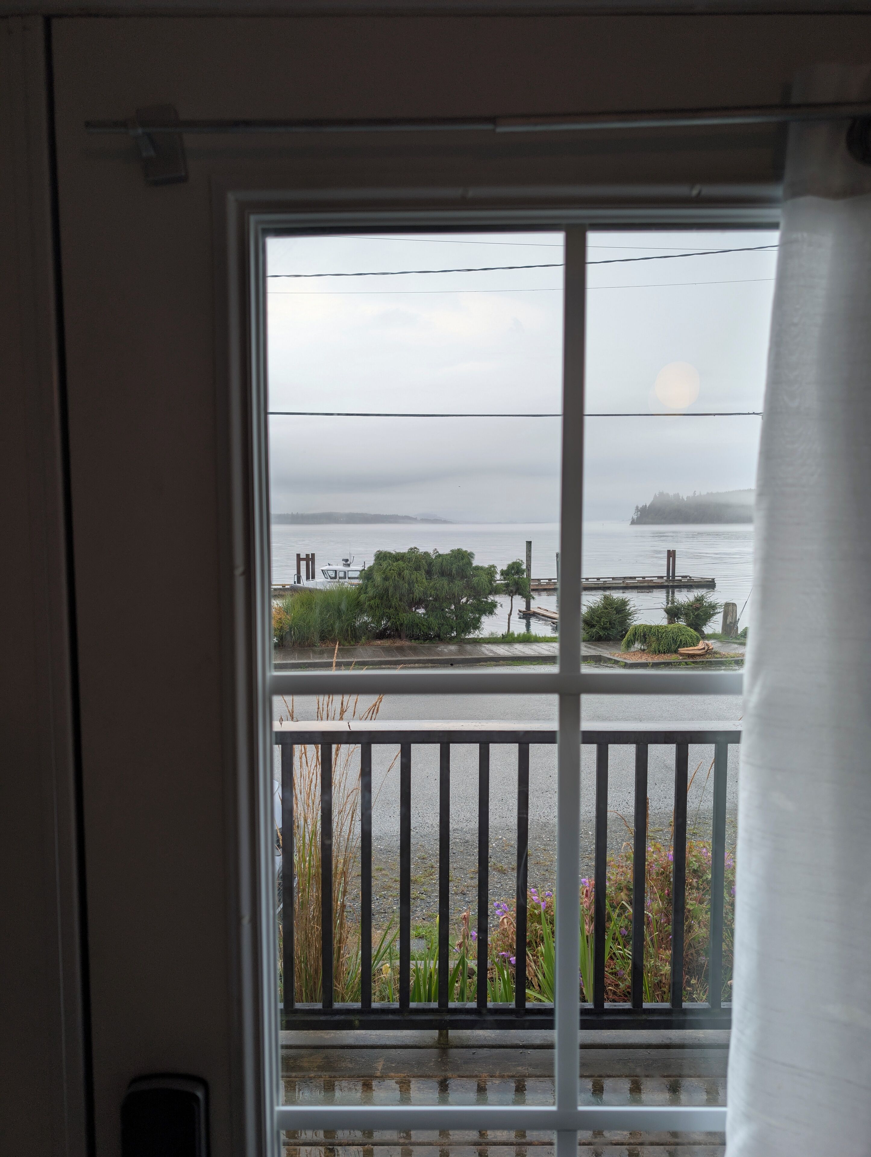 A view from a balcony with a railing, overlooking a body of water, a dock, and some greenery.