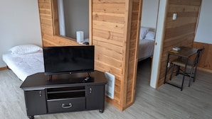 A room with a bed, a TV on a cabinet, a chair, and a wooden wall with a mirror.