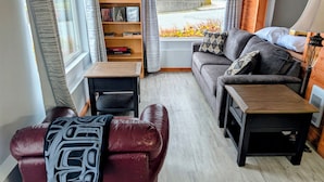 A cozy living room with a sofa, a leather armchair, a wooden coffee table, and a bookshelf.