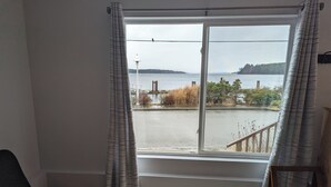 A room with a large window overlooking a body of water, a chair, and a wooden bench.
