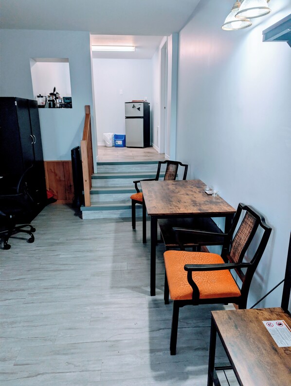 Una sala de conferencias con una mesa y sillas de madera, una kitchenette al fondo y una escalera que sube a otro piso.