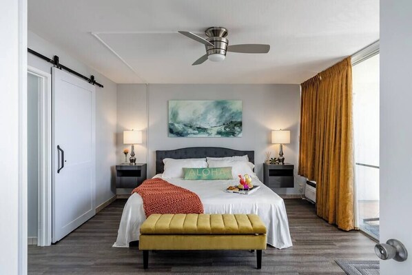 A hotel room with a bed, bedside lamps, a ceiling fan, a painting, and a window with curtains.