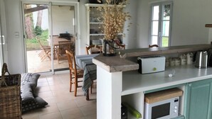A kitchen with a built-in microwave, a toaster, and a coffee maker on the counter. There is a dining table with chairs and a wicker sofa. - Individual house .  (Le Bois plage)
