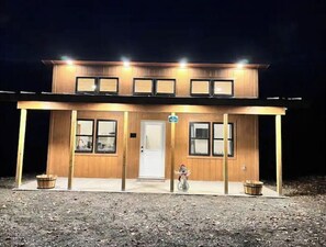 Ein zweistöckiges Holzhaus mit Veranda, zahlreichen Fenstern und einer Tür.