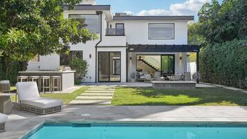 A modern two-story house with a swimming pool, outdoor seating, and a covered patio area.