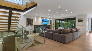 Een moderne woonkamer met een grote grijze bank, een flatscreen televisie en een trap met glazen leuning.
