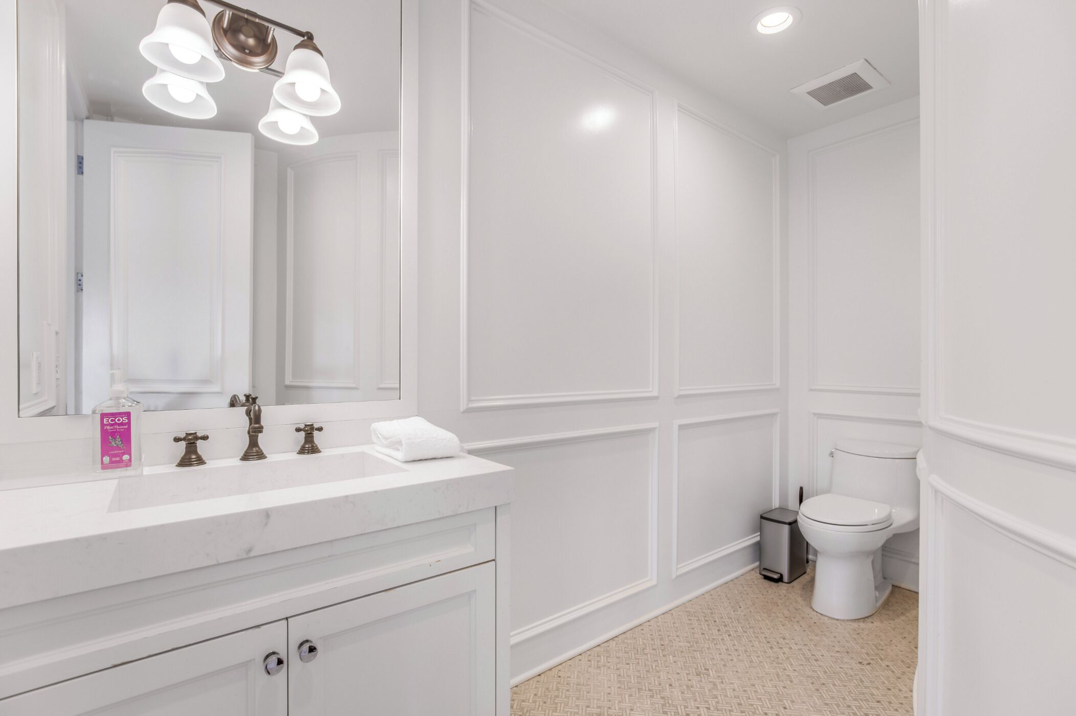 A bathroom with a white vanity, a mirror, a sink, and a toilet.