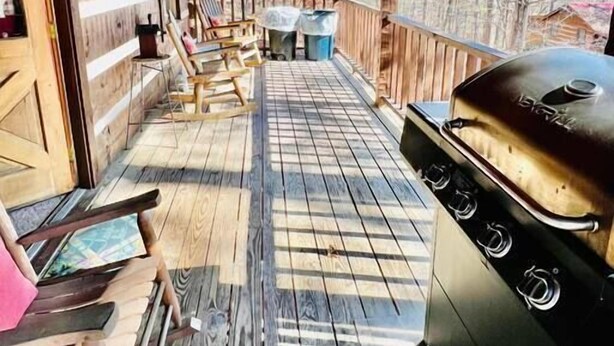 Une terrasse en bois couverte, équipée d’un barbecue, de chaises et offrant une vue sur les arbres.