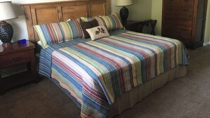 Ein Schlafzimmer mit einem hölzernen Kopfteil, einer gestreiften Bettdecke, einem Nachttisch mit Lampe und einer Kommode.