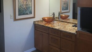 Ein Badezimmer mit einem großen Spiegel, einem Waschbecken mit Kupferbecken, Holzausbau und einem gerahmten Gemälde an der Wand.