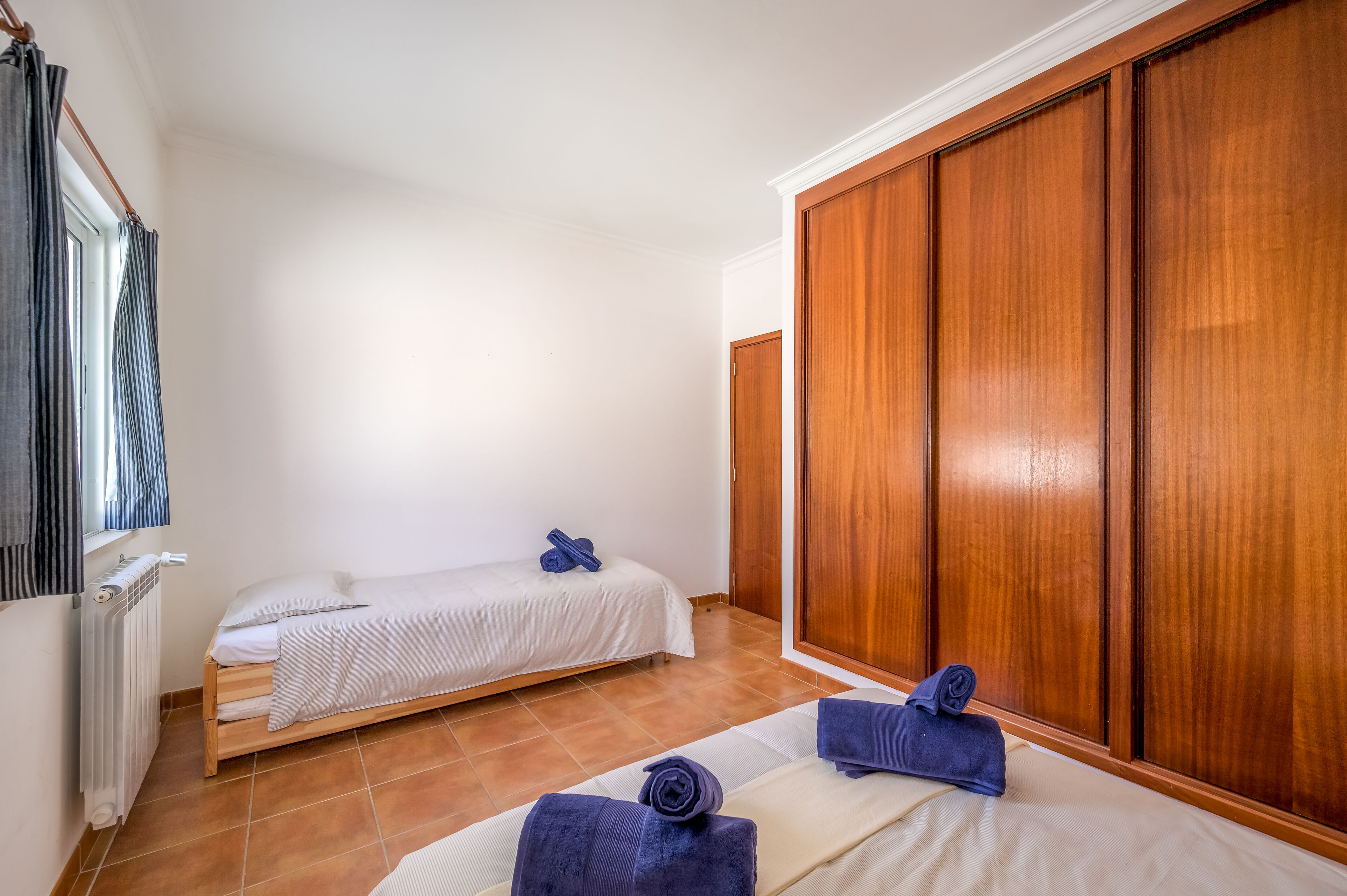 A hotel room with two single beds, a wooden wardrobe, and a window with curtains.