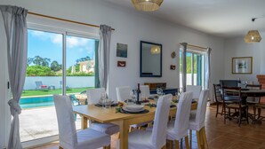A dining area with a large table set for six, white chairs, and a view of a swimming pool and garden. - QuietPrivateVilla - superwiffi (Lagos)