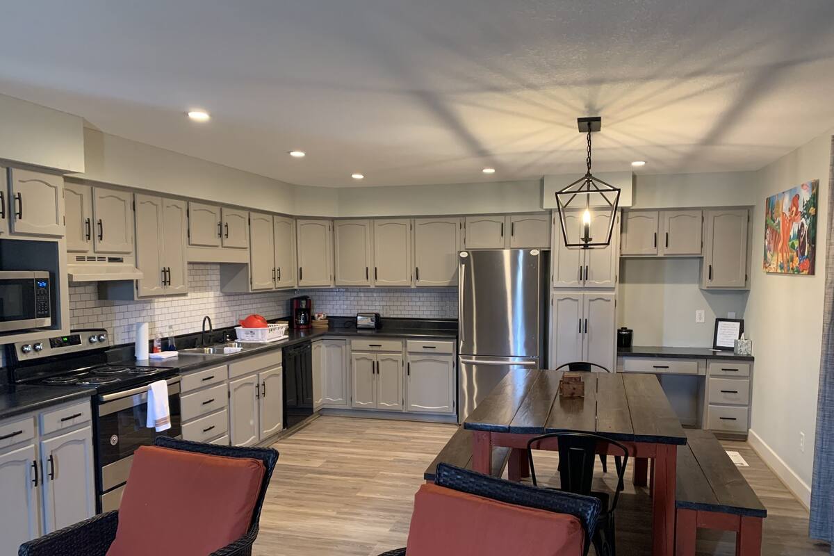 A modern kitchen with white cabinets, stainless steel appliances, and a wooden dining table.