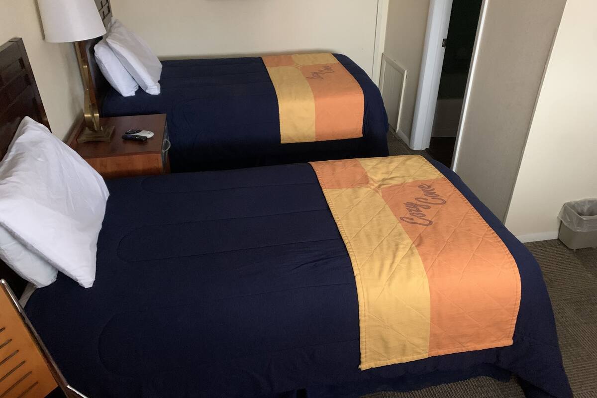 A hotel room with two beds, each with a blue and orange blanket, a nightstand with a lamp, and a framed sign on the wall.