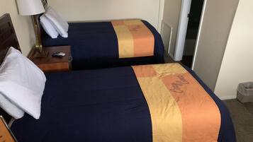 Une chambre d’hôtel avec deux lits, chacun recouvert d’une couverture bleue et orange, une table de chevet avec une lampe et un panneau encadré accroché au mur.