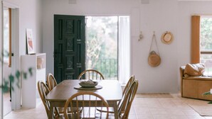 A dining area with a wooden table and chairs, a bowl of fruit, and a view of the outdoors through a door. - Vintage Charm by Number Sixteen Beach | 🐶 friendly (Rye)