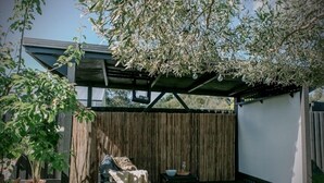 A covered outdoor patio with a wooden fence, a seating area with a bench and cushions, and a potted plant. - Vintage Charm by Number Sixteen Beach | 🐶 friendly (Rye)