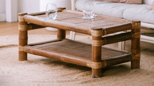 A rattan coffee table with two glasses of water, a white sofa with a pink pillow, and a potted plant in a white pot. - Vintage Charm by Number Sixteen Beach | 🐶 friendly (Rye)
