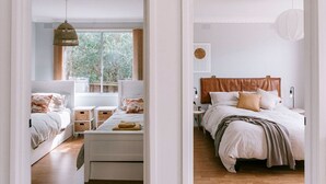 A bedroom with a bed, bedside tables, a hanging light, and a window with curtains. - Vintage Charm by Number Sixteen Beach | 🐶 friendly (Rye)