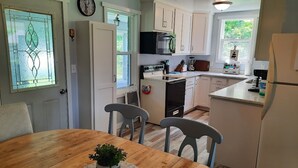 A kitchen with white cabinets, a wooden dining table with two chairs, a refrigerator, and a microwave. - Remodeled country farmhouse, 3 min drive from Mississippi River, Peaceful/Clean. (Genoa)