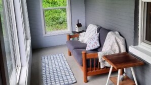 A cozy porch with a wooden bench, a small table, and a window with a view of greenery. - Remodeled country farmhouse, 3 min drive from Mississippi River, Peaceful/Clean. (Genoa)