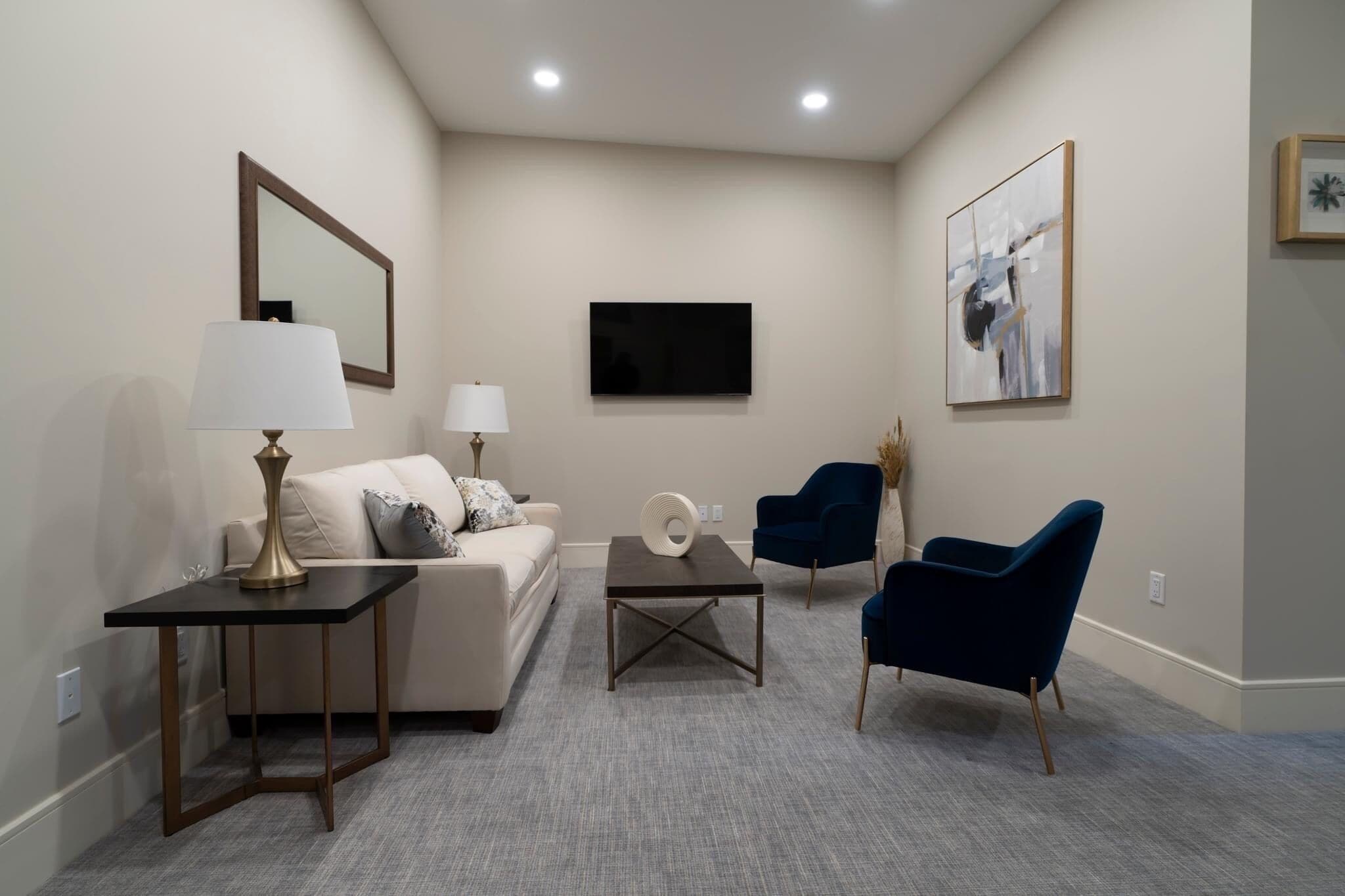 Un salon moderne comprenant un canapé, deux fauteuils, une table basse, un téléviseur et une lampe.