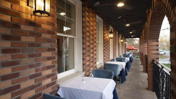 Fachada de ladrillo con terraza, mesas cubiertas con manteles blancos y paredes de ladrillo.