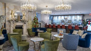 Un vestíbulo con sillones tapizados en tonos verde y azul, un árbol de Navidad y una zona de bar con taburetes rojos.