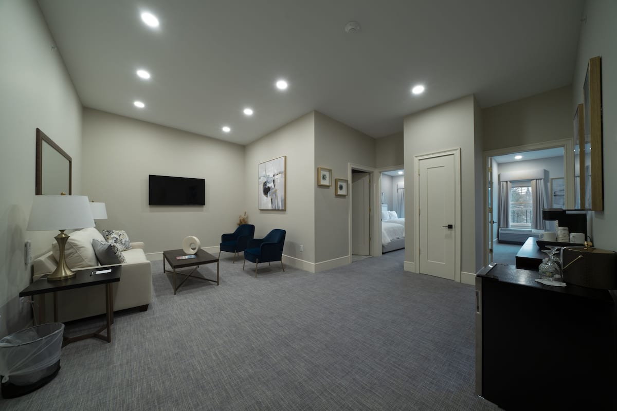 A hotel room with a sofa, two chairs, a desk, a TV, and a bed.
