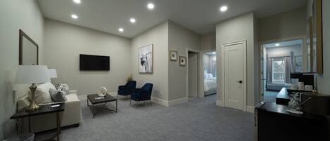 Habitación de hotel con sofá, dos sillas, escritorio, televisión y cama.