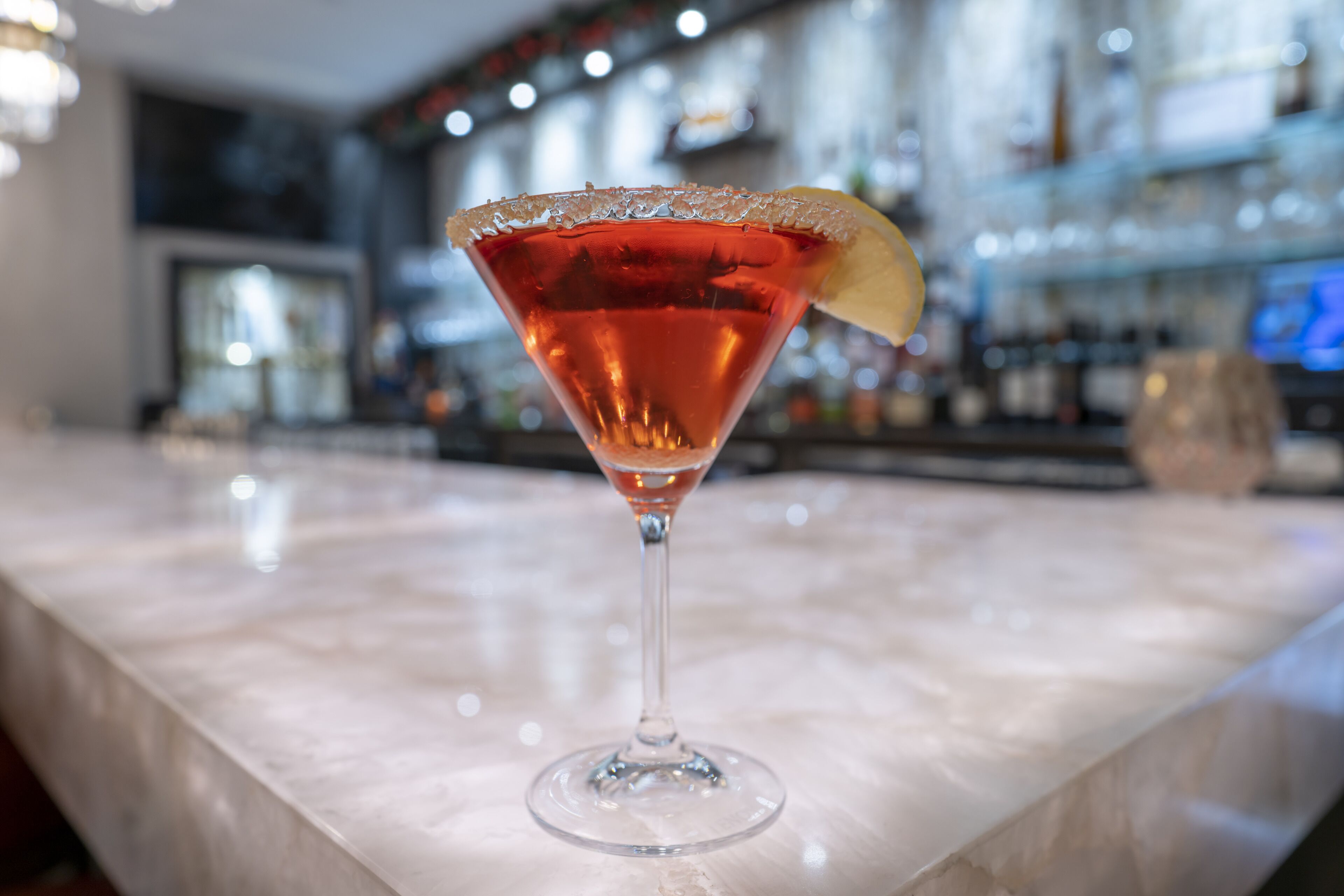 Una copa de martini con un adorno de limón sobre una barra de mármol.
