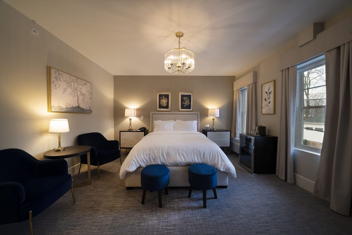 A hotel room with a large bed, two bedside tables with lamps, a desk with a chair, and a large window with curtains.