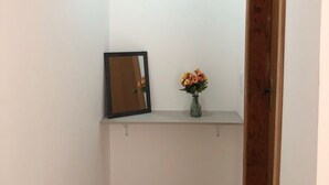 Ein schmaler Flur mit einer Holztür rechts, einer kleinen Ablage mit einem Blumenstrauß und einem Paar Schuhen auf dem Boden.
