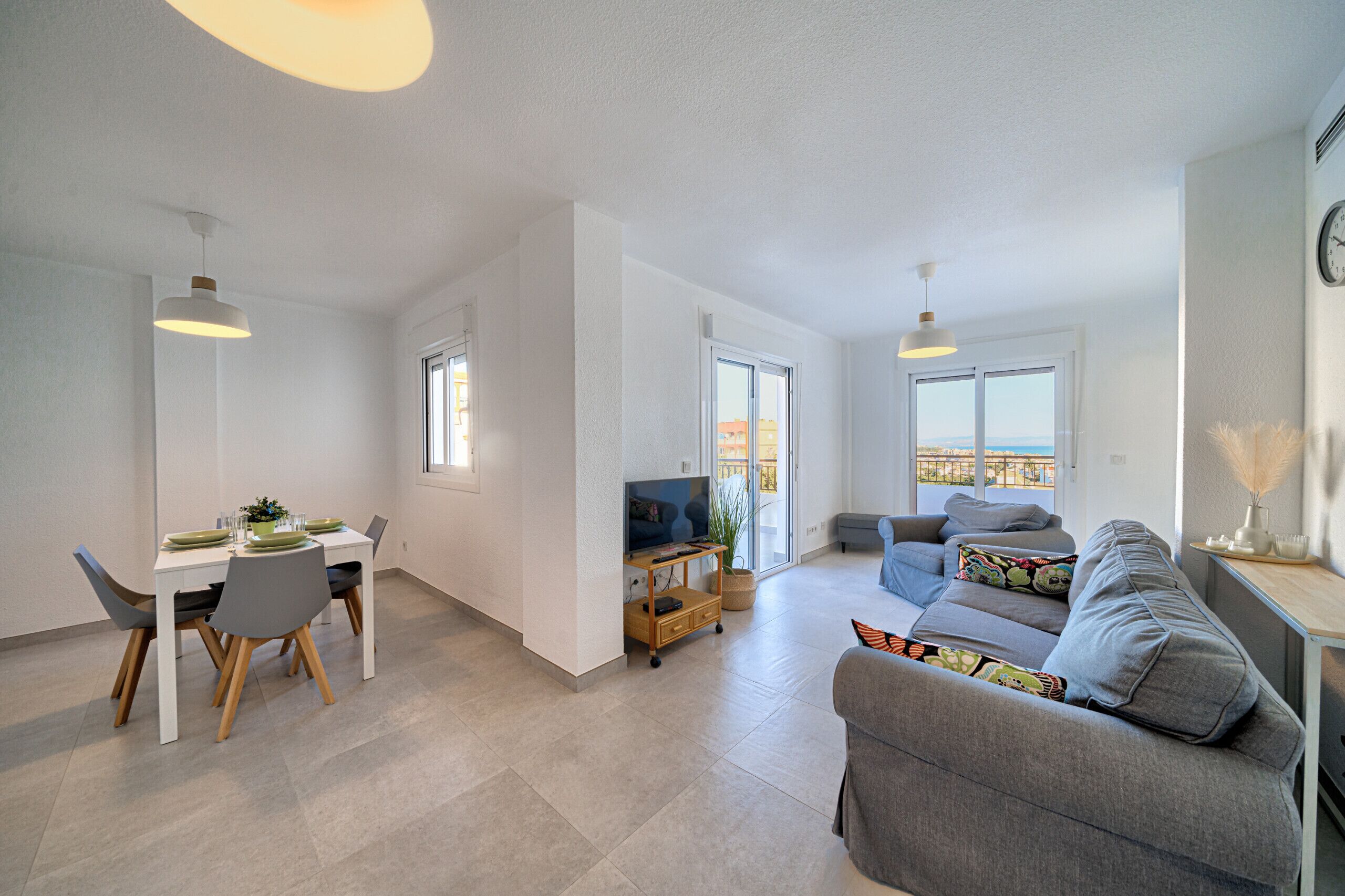 A spacious living area with a dining table, grey sofa, and a TV.