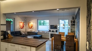 A modern kitchen with a wooden island, a dining area with wicker chairs, and a living room with a sofa and artwork. - Hexenglück Stylish apartment in the center of Hahnenklee (Goslar)