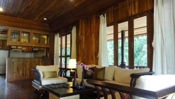 A cozy living room with a sofa, a coffee table, and a dining area with wooden furniture and a view of greenery outside. - Handcrafted Lodge short walk from Mae Nam beach (Koh Samui)
