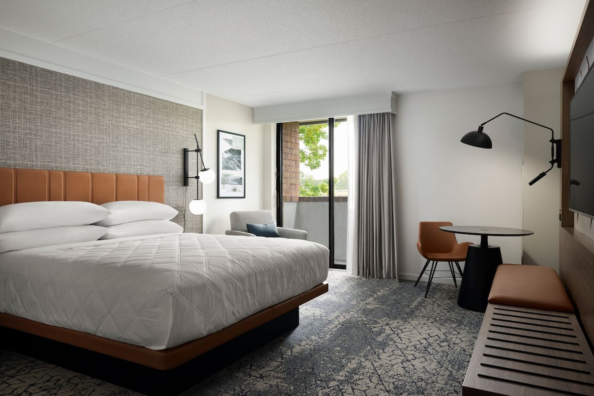Une chambre d’hôtel avec un grand lit, un bureau, une chaise, une petite table et une fenêtre avec des rideaux.