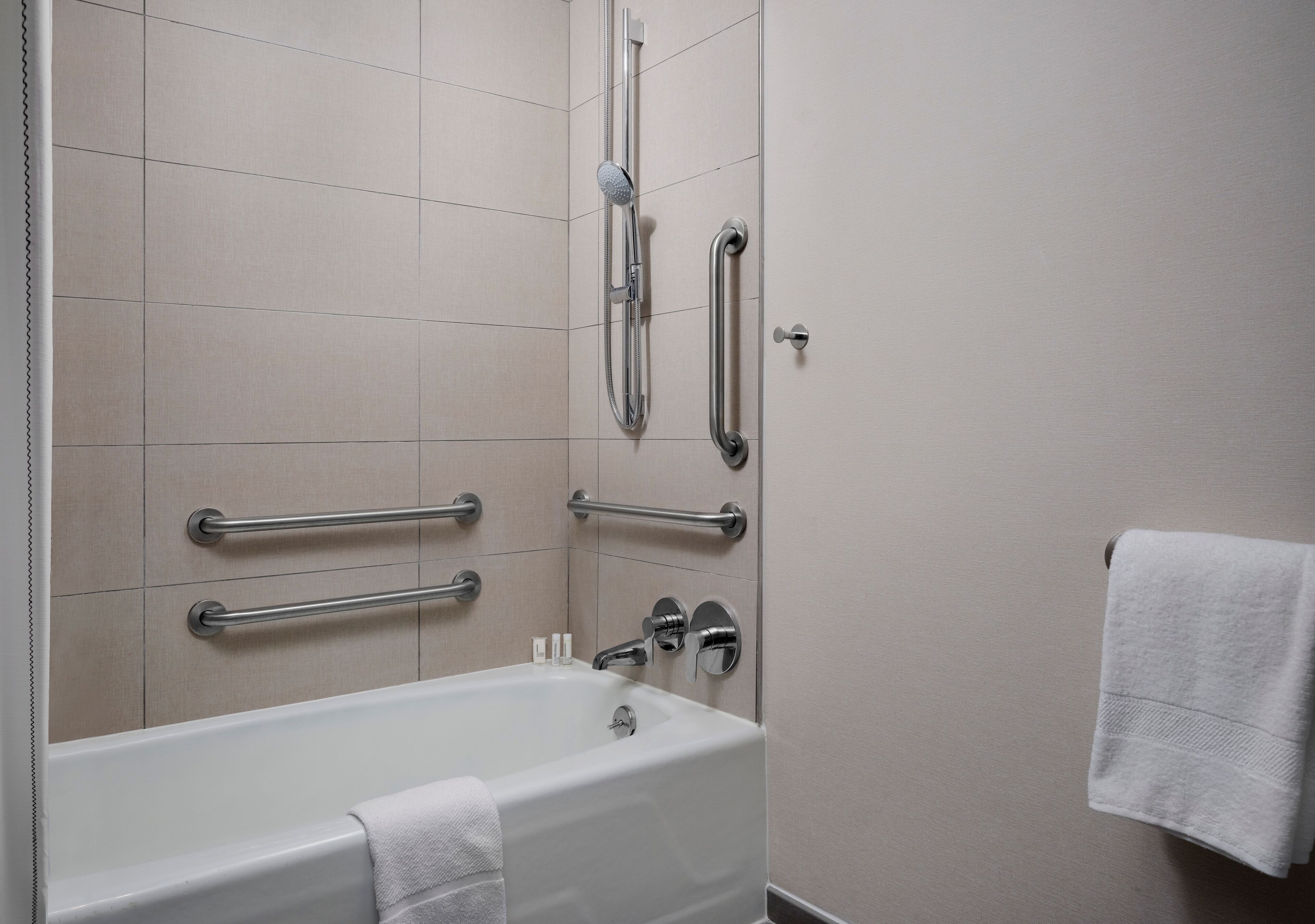 Une salle de bain moderne équipée d’une baignoire, de barres d’appui, d’un pommeau de douche et d’un porte-serviettes.