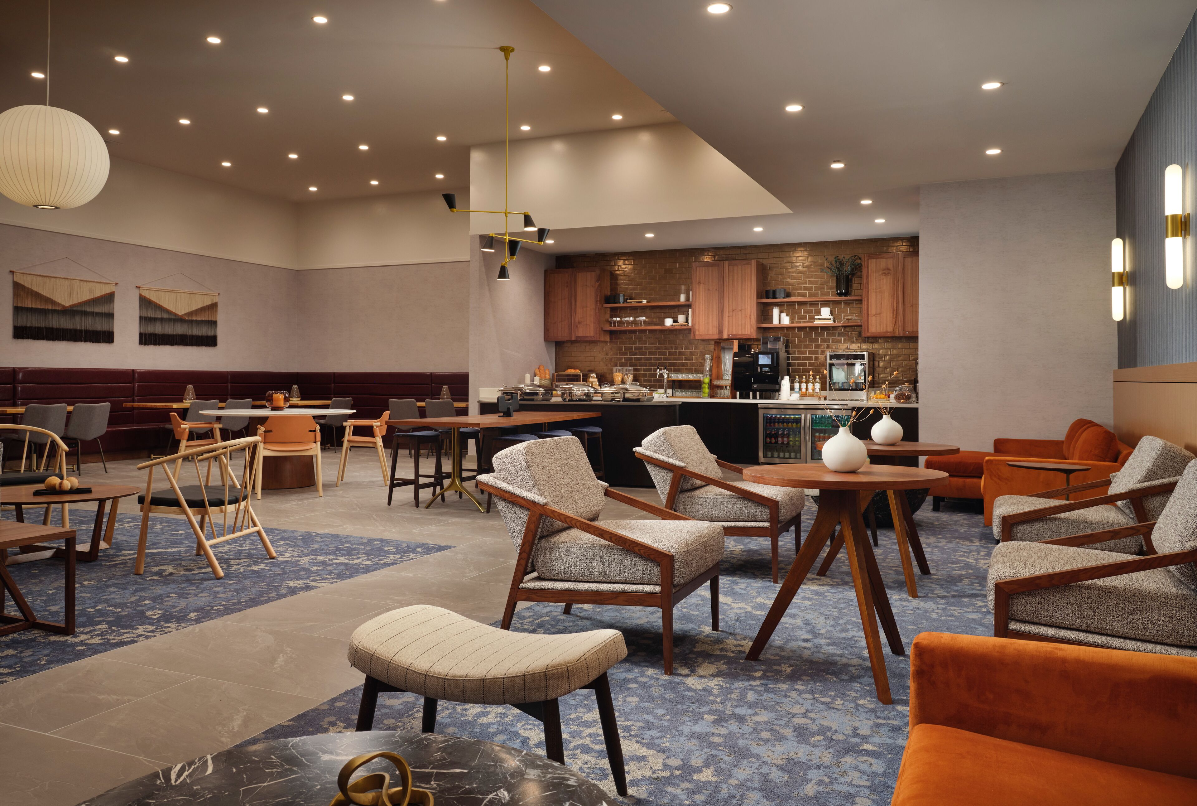 A spacious lounge area with multiple seating options, a bar, and a kitchen area in the background.