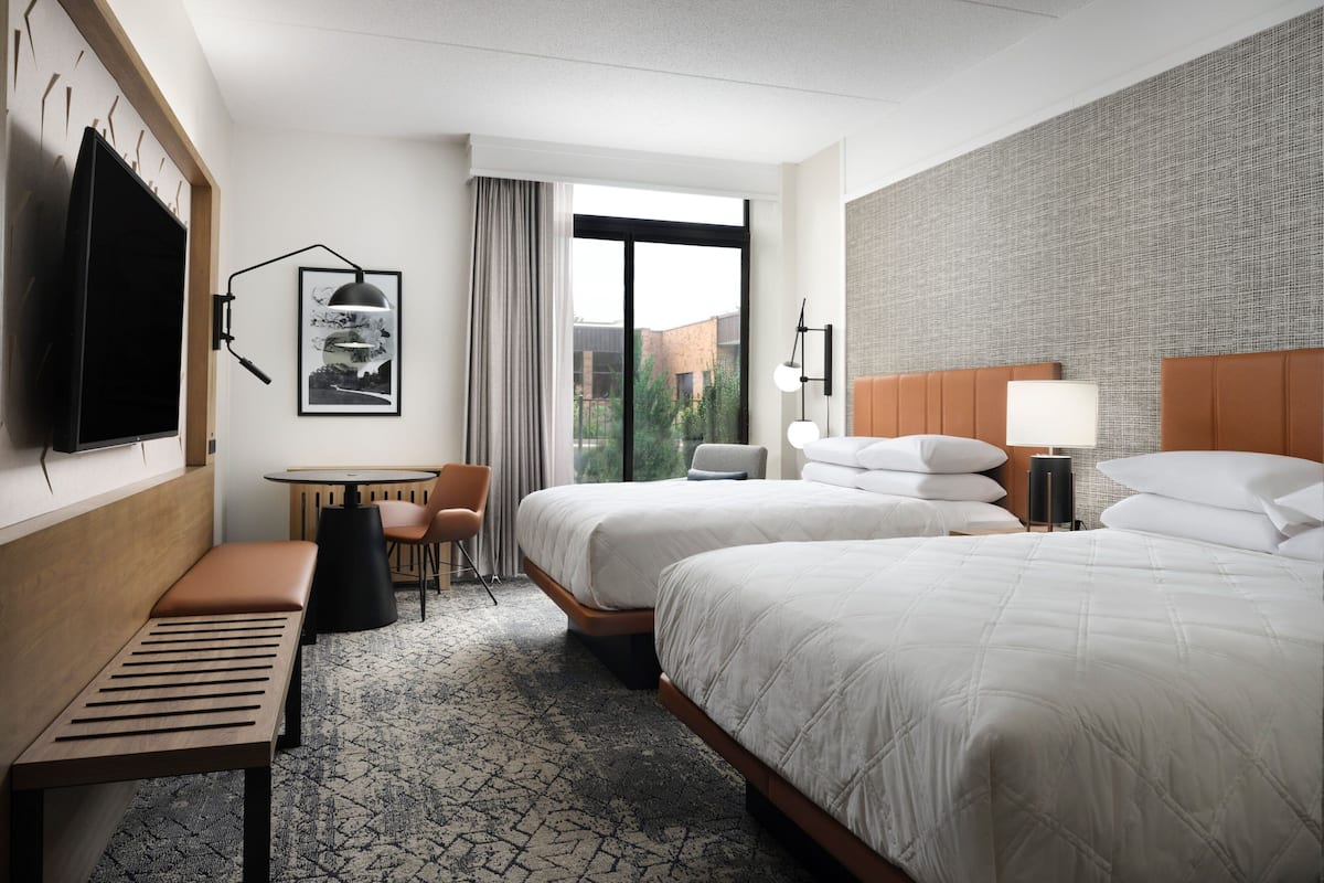 Une chambre d’hôtel avec deux lits, un banc, une table et un téléviseur.