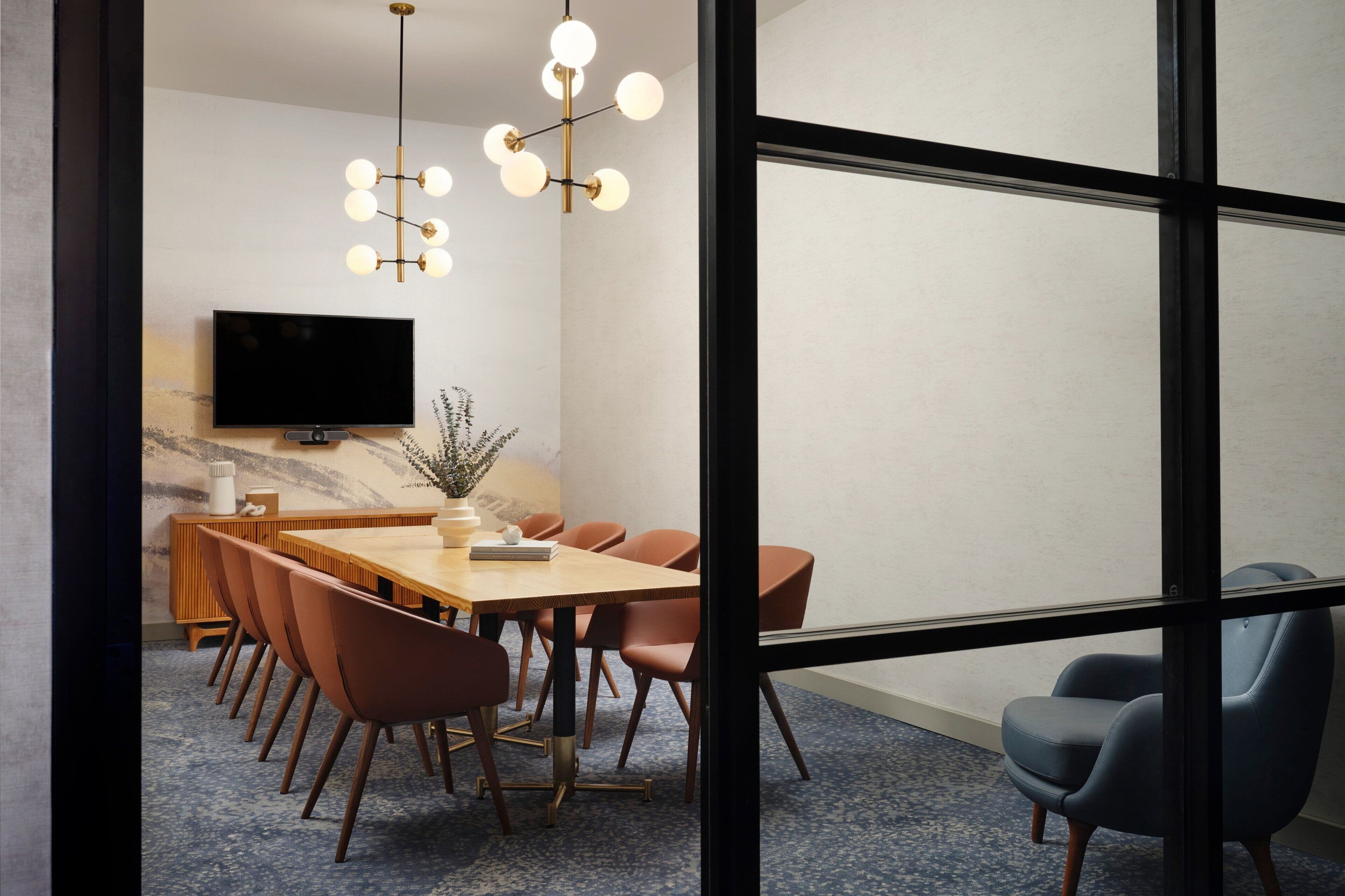 A conference room with a long table, several chairs, a television, and a modern chandelier.