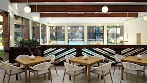 A restaurant with a long counter, white chairs, and large windows overlooking a pool. - Sheraton Grand Rapids Airport Hotel (Grand Rapids)
