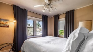 A hotel room with a bed, a ceiling fan, a window with curtains, a wall-mounted lamp, and a poster on the wall. - House in Prime Belmont Heights Near Beach w/ Gym and Garage (Long Beach)