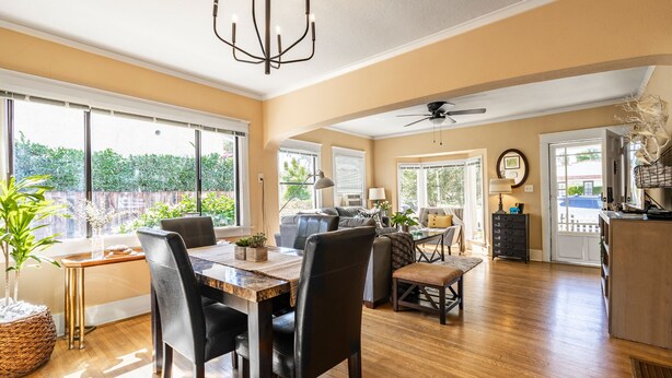 A spacious living area with a dining table, chairs, and a sofa. There are large windows providing natural light and a view of the outdoors. - House in Prime Belmont Heights Near Beach w/ Gym and Garage (Long Beach)