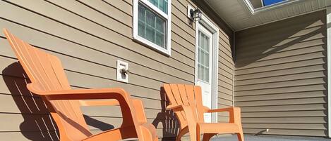 Two orange Adirondack chairs outside a beige house with a window and a door.